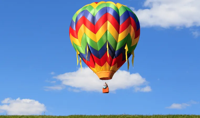 A hot air balloon floats above the ground on a sunny day.