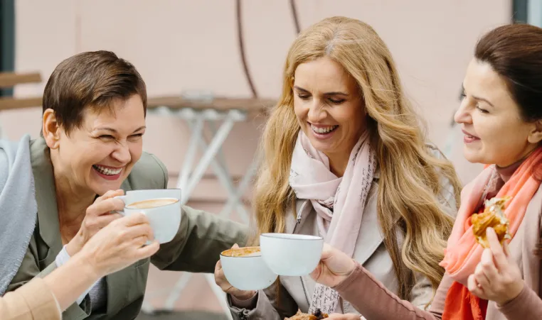 A group of women laugh as they eat outside.